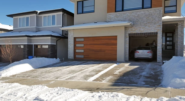 Modern house with a sleek wooden garage door, snowy driveway. -modern garage doors